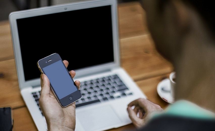 Person holding smartphone in front of a laptop